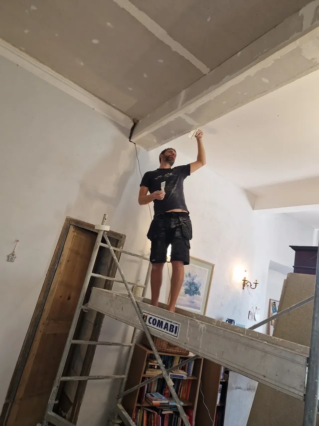 Volunteer plastering a ceiling from a scaffold tower